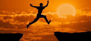 Person Jumping between two cliffs with the sun behind him.