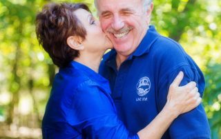 Beautiful spring background. Wife in bright blue blouse kissing her husbands cheek. Husband is in a bright blue shirt with a big smile on his face.
