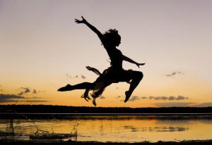 Inspirational Fitness Testimony from a Charlotte Leader, a shadow of a girl jumping like a dancer, she's in front of a lake at sunset