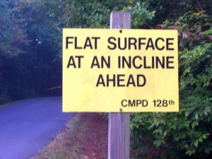 Retired CMPD Officer Becomes Fitness Coach, yellow sign on a trail that says "Flat Surface at an incline ahead CMPD 128"