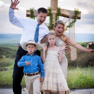 FiTness Testimony from a Professional Athlete, family of four posing with silly faces at a wedding in front of a cross