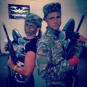 FiTness Testimony from a Professional Athlete, husband and wife in army gear and war paint posing with guns back to back