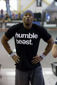 This is a super fit Christian leader you MUST get to know, athlete breathing with hands on hips, in black tshirt that says "humble beast"