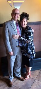 Today's Spotlight Athlete, Pastor Brent Watts, pastor in grey suit standing next to beautiful wife in multicolored top with hair all done up