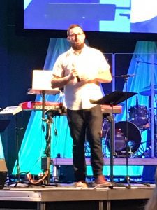 Pastor Compares Physical Training to Spiritual Training through 1 Timothy, Pastor David Miller in the pulpit in a white short sleeve dress shirt and jeans holding the microphone