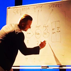 Pastor Brian Duley's FiT-Testimony, Brian in a black sports coat writing on a whiteboard, teaching in a Sunday sermon
