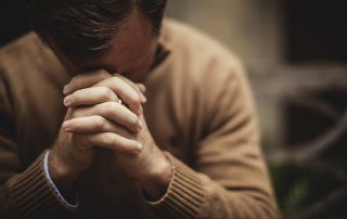 April is Stress Awareness Month, a pastor in a cream colored sweater praying looking stressed